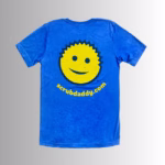 Image Description: A promotional product image showing the back of the royal blue short-sleeve t-shirt set against a neutral gradient background, featuring a large yellow smiley-face graphic with dark blue outlines and facial features above the yellow URL text "scrubdaddy.com"