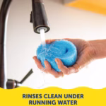 Image Description: A person's hands holding a blue Scrub Daddy sponge under running water from a kitchen faucet. Text at the bottom reads, "RINSES CLEAN UNDER RUNNING WATER".