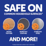 A product infographic set against a dark blue background with white text that reads "Safe on Common Household Surfaces* and More!", featuring three circular image samples showing the orange smiley-face sponge safe for use on wood texture, nonstick coating, and stainless steel.