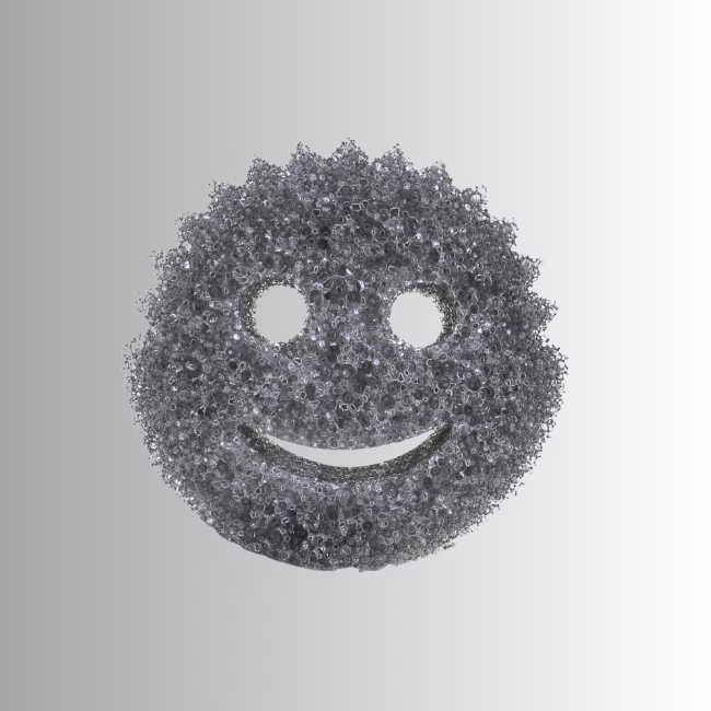 Scrub Daddy Style Hero Image Description: A promotional product hero image of a classic smiley-face scrubbing sponge in a textured metallic dark grey or charcoal finish, set against a neutral gradient background.