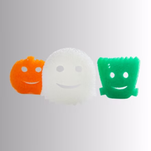 Scrub Daddy Halloween Shapes sponges lined up in a row against a clean white background. From left to right, the sponges feature an orange pumpkin shape with a stem, a white ghost shape with a jagged bottom edge, and a green Frankenstein's monster shape with stitch details on the forehead.