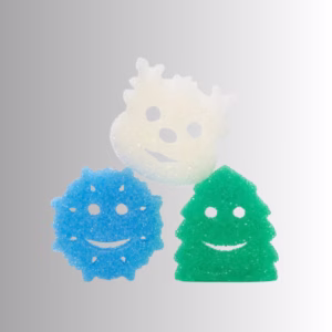 Image Description: Three winter-themed Scrub Daddy and Scrub Mommy sponges arranged against a neutral gradient background, featuring a white polar bear sponge at the top, a blue snowflake sponge on the bottom left, and a green Christmas tree sponge on the bottom right, each with a smiling face cutout.