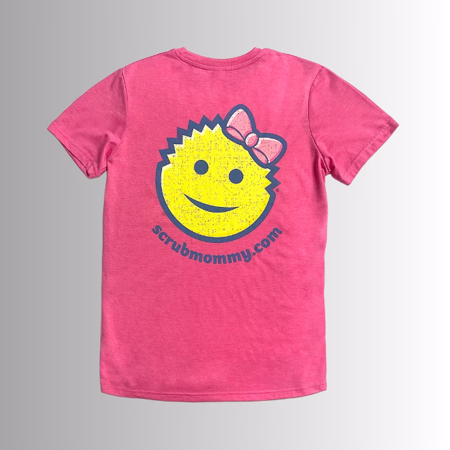 Image Description: A promotional product image showing the back of the vibrant pink short-sleeve t-shirt set against a neutral gradient background, featuring a large yellow smiley-face graphic wearing a pink bow, outlined in dark blue, above the purple URL text "scrubmommy.com".