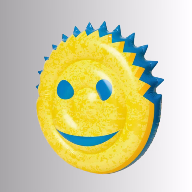 Image Description: An angled perspective product shot of the inflatable yellow smiley-face pool float set against a neutral gradient background, highlighting its puffed, rounded shape, blue facial features, and the distinct blue scalloped border.