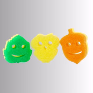 Image Description: Three autumn-themed Scrub Daddy and Scrub Mommy sponges lined up horizontally against a neutral gradient background, featuring a green leaf on the left, a yellow textured shape in the middle, and an orange acorn on the right, each with a smiling cutout face.
