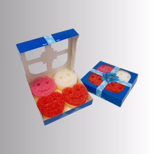 Image Description: Two blue gift-wrapped boxes designed for Valentine's Day displayed against a neutral gray and white gradient background. One box is closed with a light blue ribbon and a bow on top, while the second box sits open next to it, revealing four character-shaped scrub sponges inside: a pink one, a white one, and two red ones.