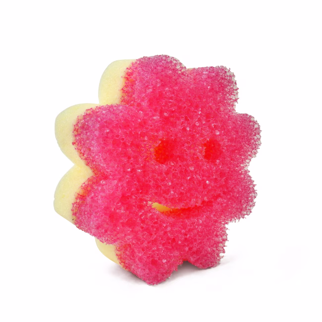 Image Description: A Pink flower-shaped Scrub Mommy sponge shown from an angled perspective against a solid white background, highlighting its dual-sided design with a textured green FlexTexture scrubbing side on the front and a yellow absorbent foam side visible along the edges.
