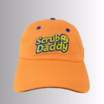 Image Description: A promotional product hero image of an orange Scrub Daddy baseball cap set against a neutral gradient background, featuring embroidered blue and yellow "Scrub Daddy" lettering on the front crown.