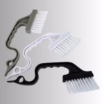 Image Description: A promotional product hero image of a set of three small cleaning brushes in gray, white, and black, set against a neutral gradient background, featuring curved ergonomic handles and angled white bristle heads.