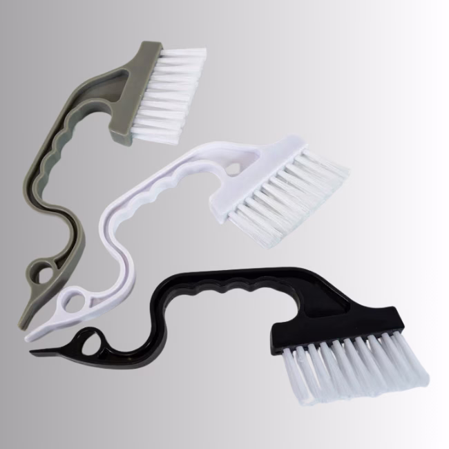 Tiny Little Brushes Hero Image Description: A promotional product hero image of a set of three small cleaning brushes in gray, white, and black, set against a neutral gradient background, featuring curved ergonomic handles and angled white bristle heads.