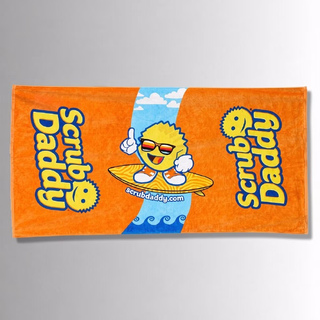 Beach Towel Image Description: A promotional product flat-lay image of a vibrant orange beach towel set against a neutral gradient background, featuring a central graphic of a smiling Scrub Daddy character wearing sunglasses and sneakers while riding a surfboard on a blue wave path, flanked by large blue and yellow "Scrub Daddy" lettering on either side.