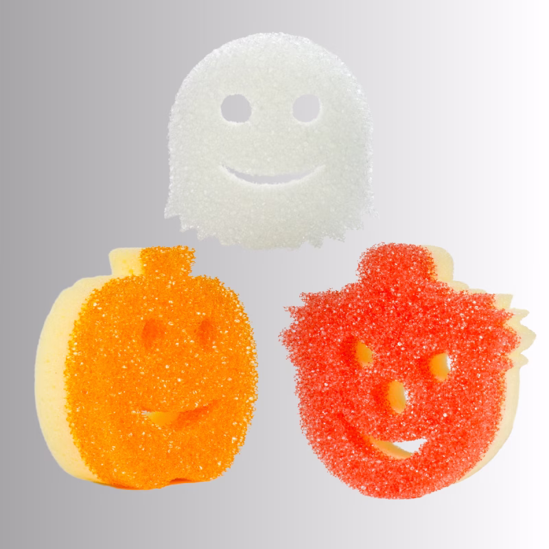 Image Description: Three Halloween-themed Scrub Mommy sponges arranged against a neutral gray and white gradient background, featuring a white ghost sponge at the top, an orange pumpkin sponge on the bottom left, and a red-textured clown or jack-o'-lantern character sponge on the bottom right.
