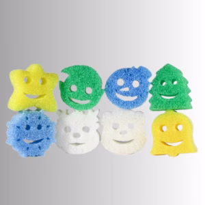 Eight holiday-themed Scrub Daddy and Scrub Mommy sponges arranged in two rows of four against a neutral background. The top row features a yellow star, a green round ornament, a blue round ornament, and a green Christmas tree. The bottom row features a blue snowflake, a white bear or polar bear, a white snowman, and a yellow bell.