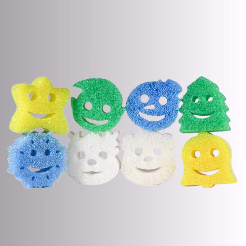 Image Description: Eight holiday-themed Scrub Daddy and Scrub Mommy sponges arranged in two rows of four against a neutral background. The top row features a yellow star, a green round ornament, a blue round ornament, and a green Christmas tree. The bottom row features a blue snowflake, a white bear or polar bear, a white snowman, and a yellow bell.