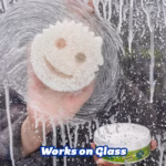Image Description: A lifestyle action shot showing a hand using a Scrub Mommy sponge with soapy water and PowerPaste to clean and scrub smudges off a glass window or surface, with an open tub of PowerPaste visible in the corner.