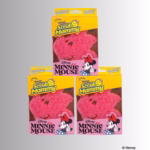 Image Description: Three product packaging boxes for a Minnie Mouse special edition Scrub Mommy 3-pack, arranged with one box centered on top and two identical boxes placed side-by-side underneath. © Disney