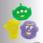 Image Description: Three character-shaped Scrub Mommy sponges arranged together: a green Alien sponge with three eye cutouts at the top, a yellow Woody sponge wearing a cowboy hat on the bottom left, and a purple Buzz Lightyear helmet-shaped sponge on the bottom right. © Disney/Pixar