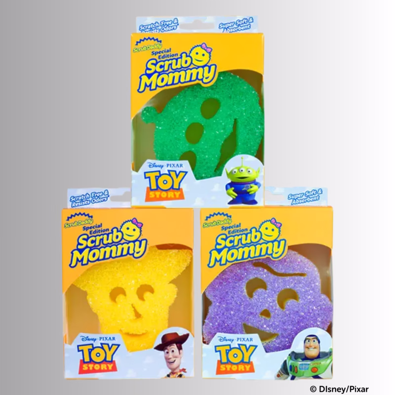 Image Description: Three individual product boxes for a Toy Story Scrub Mommy special edition set, arranged with a green Alien sponge box on top, a yellow Woody sponge box on the bottom left, and a purple-and-blue Buzz Lightyear sponge box on the bottom right. © Disney/Pixar