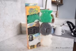 Scrub Daddy Star Wars: The Mandalorian and Grogu Sponges (3-Pack) displayed on a kitchen counter in front of a sink setup. On the left is the special edition retail box featuring Mandalorian branding. Stacked vertically to the right are the three character-shaped sponges: a green Grogu sponge at the top, a dark grey Mandalorian helmet sponge in the middle, and a white Grogu in the hover pram sponge at the bottom. The copyright "© & ™ Lucasfilm Ltd" appears in the bottom right corner.