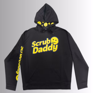 Image Description: A promotional product hero image for a black Scrub Daddy branded hoodie set against a neutral gradient background, featuring the yellow Scrub Daddy logo on the chest, matching yellow branding text down the right sleeve, and a hood interior lined with a yellow smiley face pattern.