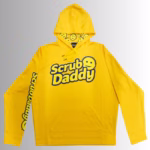 Image Description: A promotional product hero image of a bright orange Scrub Daddy hoodie set against a neutral gradient background, featuring the blue and yellow Scrub Daddy logo on the chest, matching yellow branding down the sleeve, and a hood interior lined with a yellow smiley-face pattern.