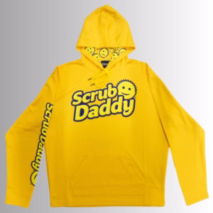 Image Description: A promotional product hero image of a bright orange Scrub Daddy hoodie set against a neutral gradient background, featuring the blue and yellow Scrub Daddy logo on the chest, matching yellow branding down the sleeve, and a hood interior lined with a yellow smiley-face pattern.