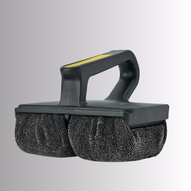 Griddle Hero Shot Image Description: A promotional product hero image set against a neutral gradient background, showcasing a black Scrub Daddy Griddle Daddy cleaning tool featuring an ergonomic handle with yellow detailing and dual textured scrubbing pads underneath.