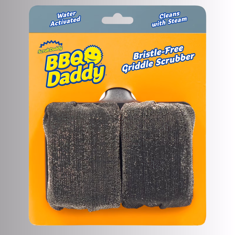 Image Description: Packaging for a Scrub Daddy BBQ Daddy Bristle-Free Griddle Scrubber, featuring a bright orange cardboard backing with blue text that reads "Water Activated," "Cleans with Steam," and "Bristle-Free Griddle Scrubber." The product itself consists of two dark, textured scrubber pads mounted on a dark handle holder.