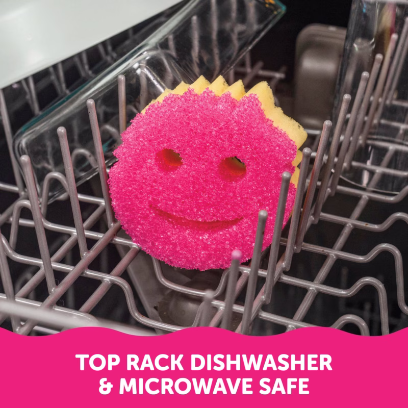 A pink and yellow dual-sided Scrub Mommy sponge resting on the grey tines of a dishwasher rack. A pink banner at the bottom contains white text reading, "TOP RACK DISHWASHER & MICROWAVE SAFE".