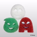 Image Description: Three character-shaped Scrub Daddy and Scrub Mommy sponges from The Nightmare Before Christmas collection arranged in a triangle against a light grey background. At the top is the white Jack Skellington sponge, on the bottom left is the green Oogie Boogie sponge, and on the bottom right is the red Sally sponge. The copyright text "© Disney" appears in the bottom right corner.