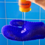 Image Description: An action product photo showing body wash being poured from the bottle onto the textured surface of the blue exfoliating mitt against a blue tiled background.