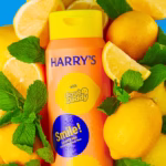 Image Description: A product photo of the Lemon & Mint body wash bottle surrounded by fresh lemons and mint leaves against a blue tiled background with soap bubbles.