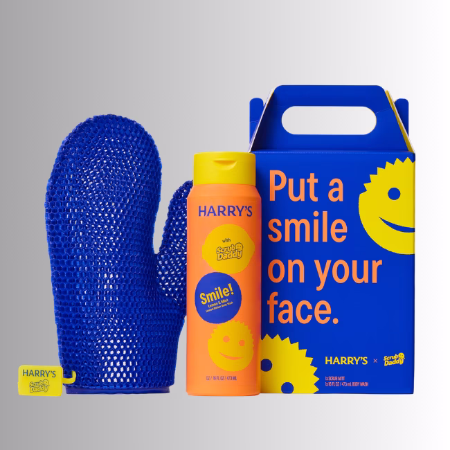 Image Description: A promotional product hero image of the Harry's x Scrub Daddy collaboration set against a neutral gradient background, featuring a blue exfoliating mitt, a 16 fl oz bottle of Lemon & Mint body wash, and a branded blue gift box with yellow smiley graphics.