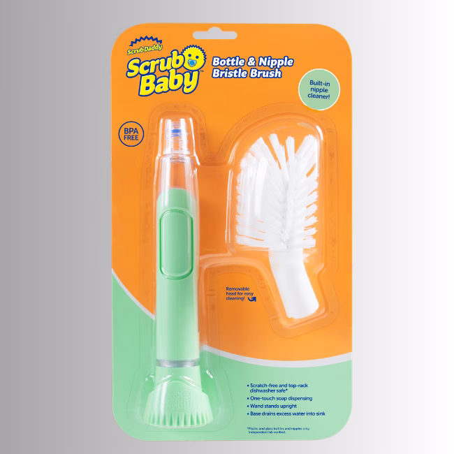 Image Description: A retail packaging product shot of the Scrub Baby Bottle & Nipple Bristle Brush set against a neutral gradient background, showcasing the orange and green blister pack containing the green soap-dispensing wand and a detachable white bristle head